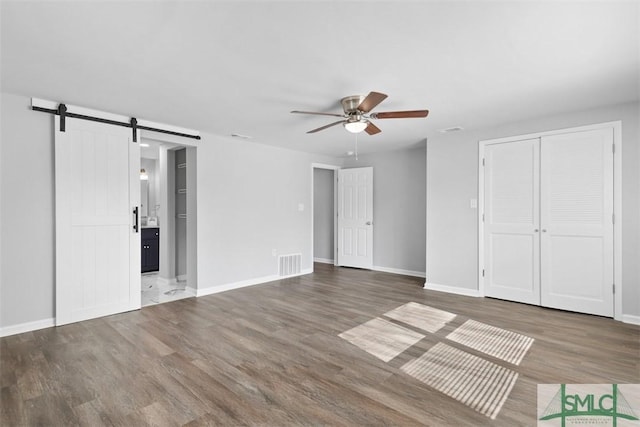 unfurnished bedroom featuring wood-type flooring, a barn door, ceiling fan, and ensuite bathroom