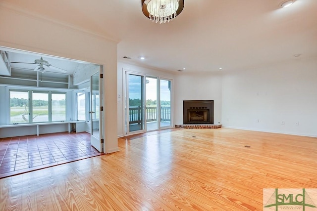 unfurnished living room featuring ceiling fan with notable chandelier, a fireplace, and light wood-type flooring