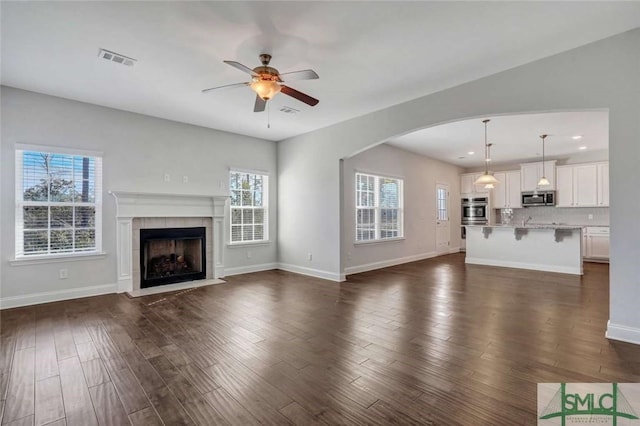 unfurnished living room featuring dark hardwood / wood-style flooring, a tiled fireplace, and ceiling fan