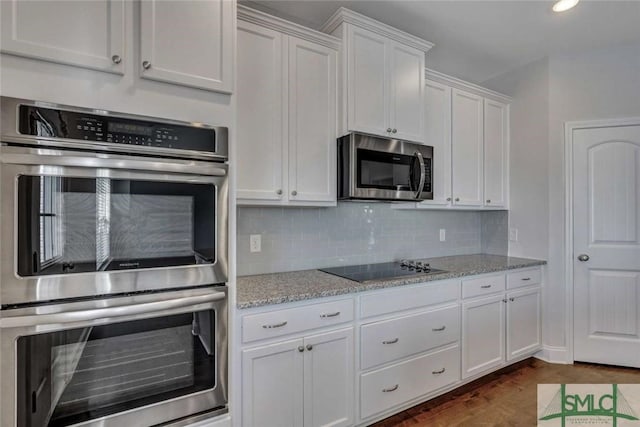 kitchen with white cabinetry, light stone counters, dark hardwood / wood-style flooring, stainless steel appliances, and decorative backsplash