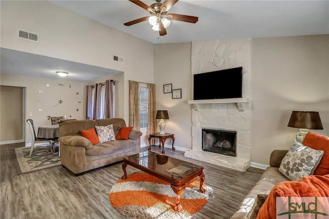 living room featuring ceiling fan, wood-type flooring, a fireplace, and high vaulted ceiling