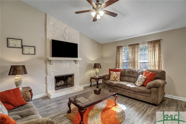 living room featuring hardwood / wood-style flooring, a stone fireplace, lofted ceiling, and ceiling fan