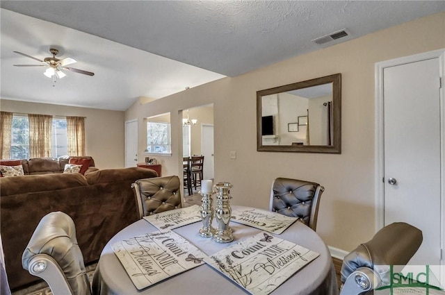 dining room with ceiling fan with notable chandelier and a textured ceiling