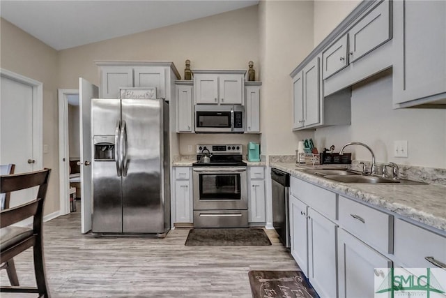 kitchen featuring lofted ceiling, sink, light stone counters, light hardwood / wood-style flooring, and stainless steel appliances