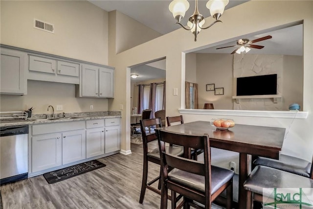 kitchen with sink, hanging light fixtures, stainless steel dishwasher, light stone countertops, and light hardwood / wood-style floors