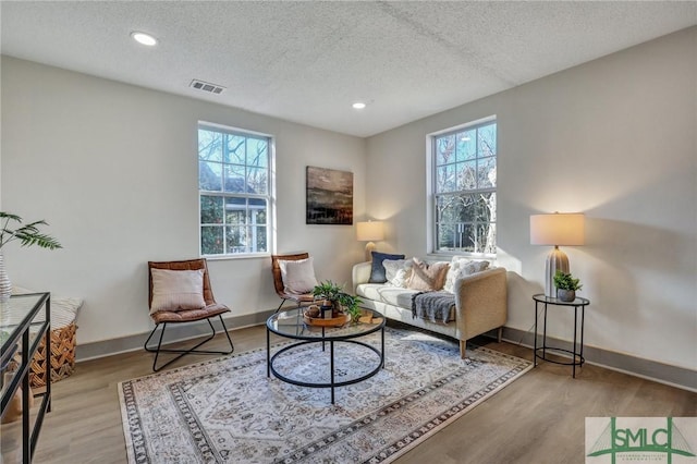 sitting room with a textured ceiling, a wealth of natural light, wood finished floors, and visible vents