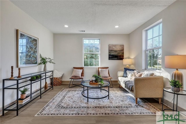 sitting room with baseboards, wood finished floors, visible vents, and a healthy amount of sunlight