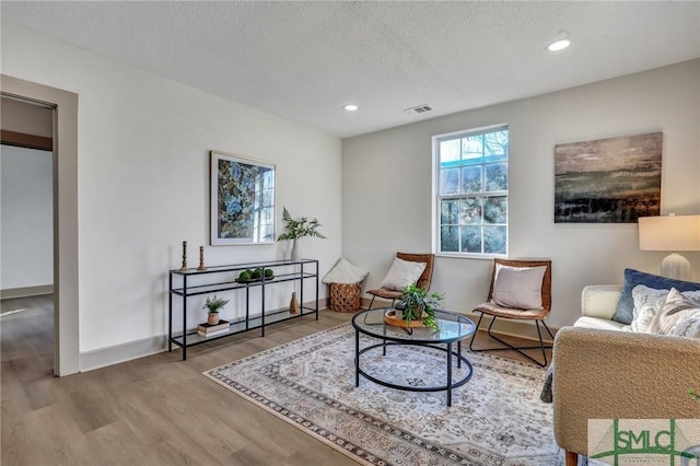 living area with a textured ceiling, wood finished floors, visible vents, and recessed lighting