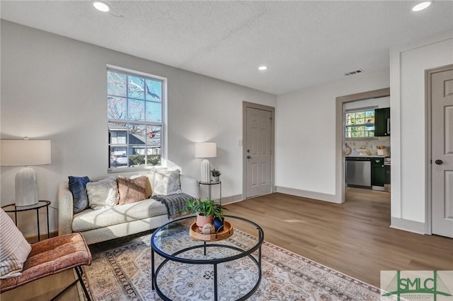 living area with baseboards, visible vents, wood finished floors, a textured ceiling, and recessed lighting