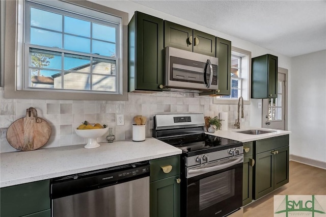 kitchen with stainless steel appliances, a sink, green cabinets, decorative backsplash, and plenty of natural light