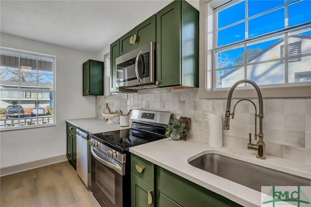 kitchen featuring plenty of natural light, appliances with stainless steel finishes, green cabinets, and a sink