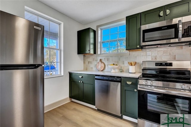 kitchen with stainless steel appliances, light countertops, green cabinetry, and backsplash