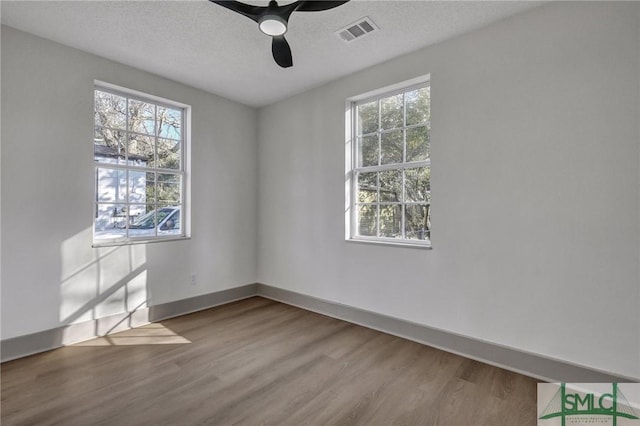 empty room featuring a textured ceiling, wood finished floors, a ceiling fan, visible vents, and baseboards