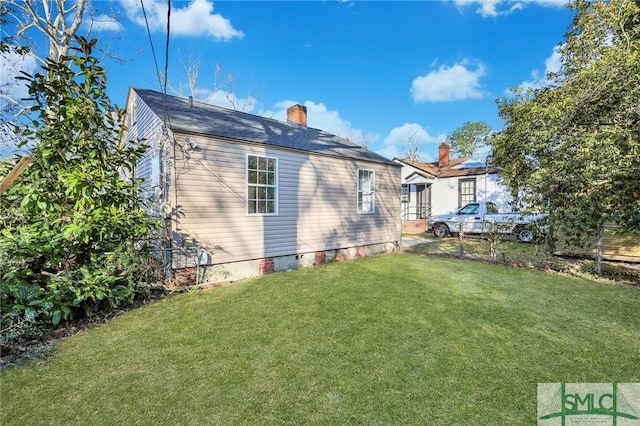 view of side of home with crawl space, a chimney, fence, and a lawn