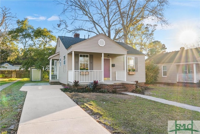 bungalow-style house featuring covered porch, a shingled roof, a chimney, and a front yard