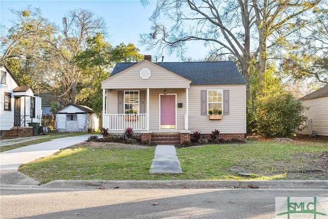 bungalow-style home with roof with shingles, a chimney, a porch, a front yard, and an outdoor structure