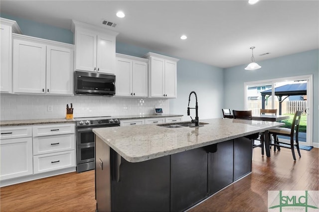 kitchen featuring sink, white cabinets, hanging light fixtures, stainless steel appliances, and a center island with sink