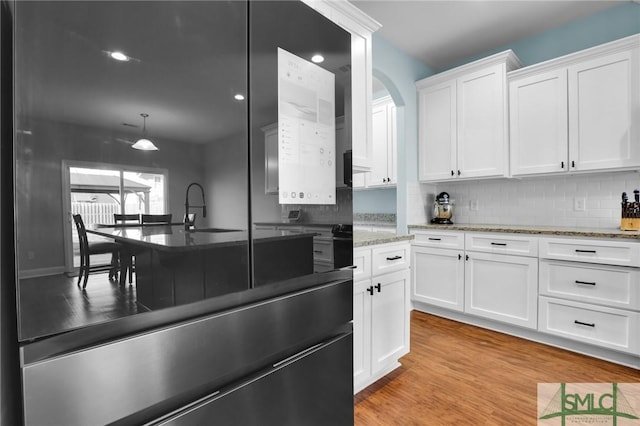 kitchen featuring pendant lighting, sink, white cabinetry, backsplash, and light hardwood / wood-style floors