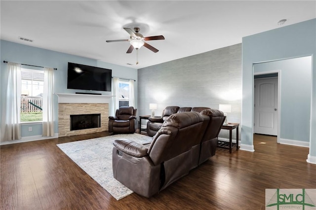 living room featuring dark hardwood / wood-style flooring, a stone fireplace, and ceiling fan