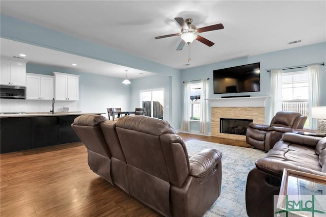 living room with a stone fireplace, ceiling fan, and light hardwood / wood-style flooring