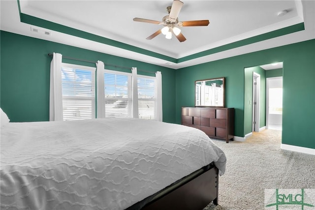 bedroom featuring a raised ceiling, connected bathroom, light carpet, and ceiling fan