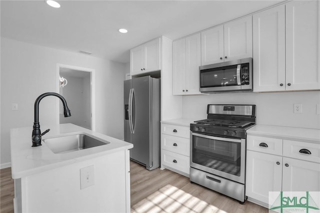 kitchen featuring sink, white cabinetry, stainless steel appliances, light hardwood / wood-style floors, and light stone countertops