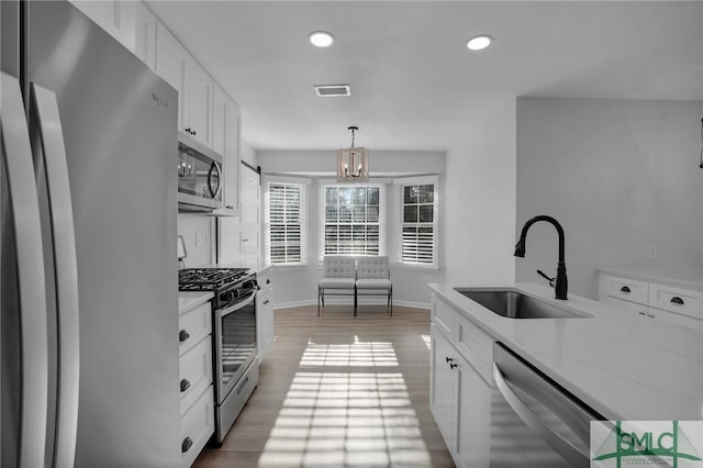 kitchen featuring sink, white cabinetry, wood-type flooring, appliances with stainless steel finishes, and pendant lighting