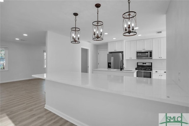 kitchen with sink, white cabinetry, hanging light fixtures, light wood-type flooring, and appliances with stainless steel finishes