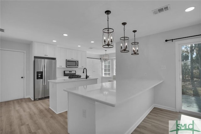 kitchen with hanging light fixtures, appliances with stainless steel finishes, kitchen peninsula, a healthy amount of sunlight, and white cabinets