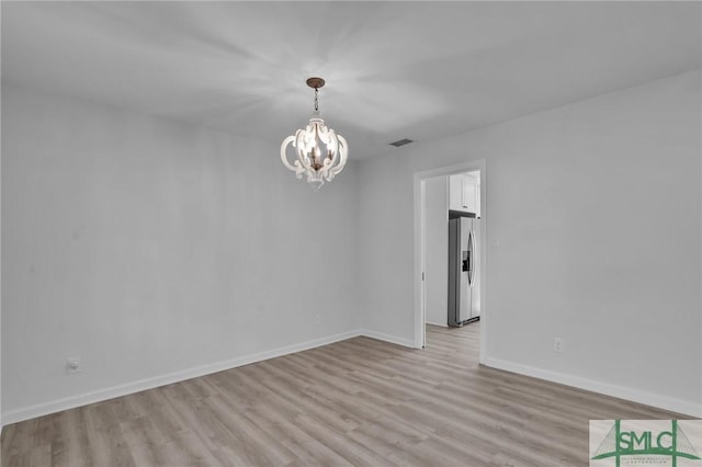 empty room with a chandelier and light wood-type flooring