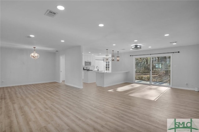 unfurnished living room with an inviting chandelier, sink, and light hardwood / wood-style flooring