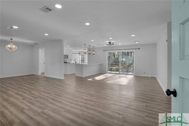 unfurnished living room featuring a chandelier, sink, and light wood-type flooring