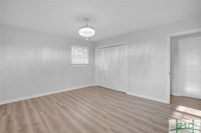 unfurnished bedroom featuring a notable chandelier, light hardwood / wood-style floors, and a closet