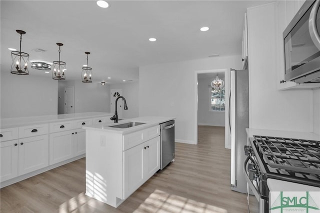 kitchen with pendant lighting, sink, stainless steel appliances, an island with sink, and white cabinets