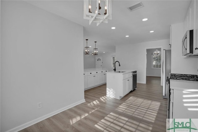 kitchen featuring sink, hanging light fixtures, stainless steel appliances, an island with sink, and white cabinets