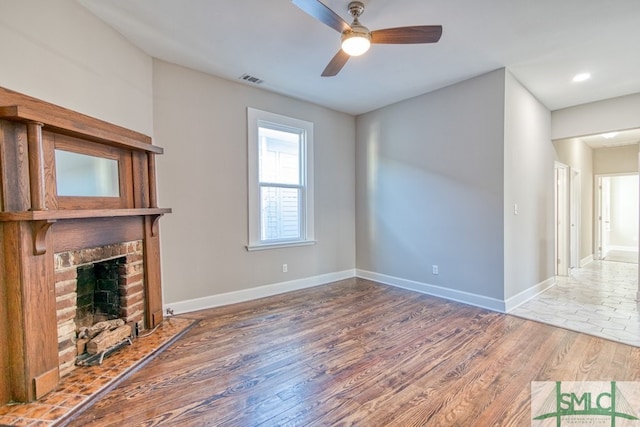 unfurnished living room featuring a brick fireplace, wood-type flooring, and ceiling fan