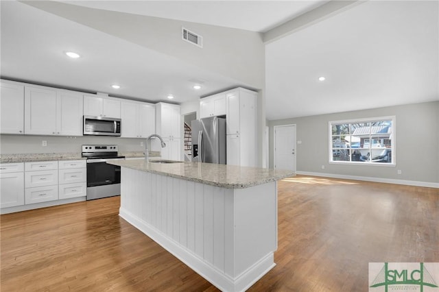 kitchen featuring light hardwood / wood-style flooring, vaulted ceiling with beams, stainless steel appliances, light stone counters, and white cabinets