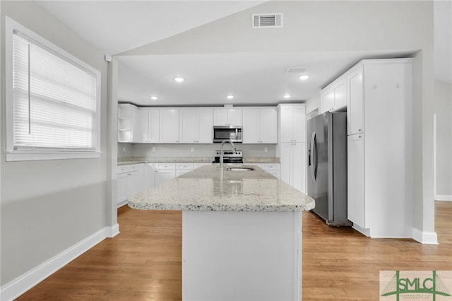 kitchen featuring sink, appliances with stainless steel finishes, light stone countertops, white cabinets, and a center island with sink