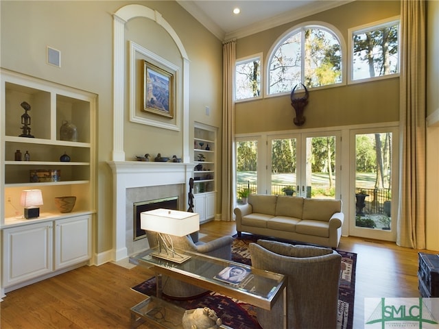 living room featuring built in shelves, ornamental molding, a towering ceiling, a tiled fireplace, and hardwood / wood-style floors