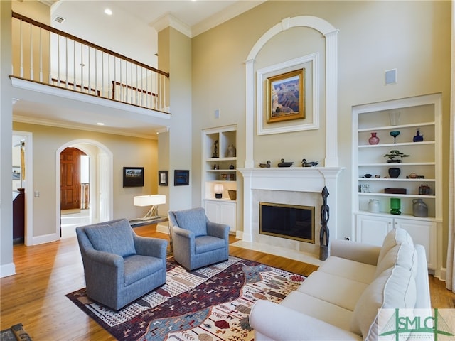 living room with crown molding, built in features, a high end fireplace, light hardwood / wood-style floors, and a high ceiling