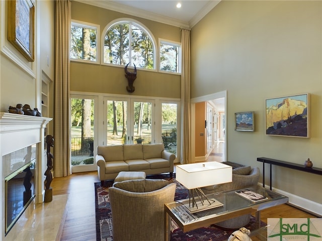 living room with crown molding, a high ceiling, wood-type flooring, a high end fireplace, and french doors