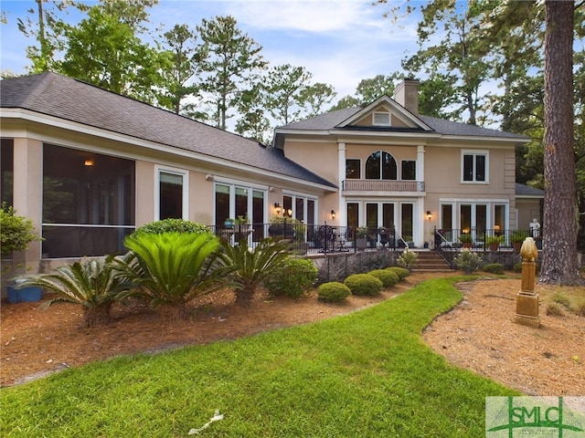 rear view of house featuring a balcony, a sunroom, and a yard