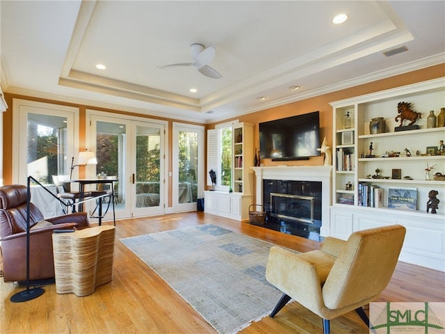 living room featuring a raised ceiling, crown molding, and light hardwood / wood-style flooring