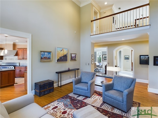 living room with a towering ceiling, ornamental molding, and light hardwood / wood-style flooring