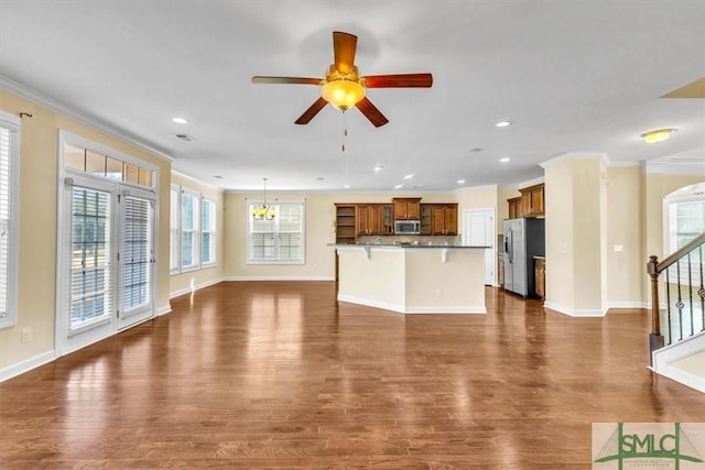 unfurnished living room featuring dark wood-type flooring, ornamental molding, and ceiling fan with notable chandelier