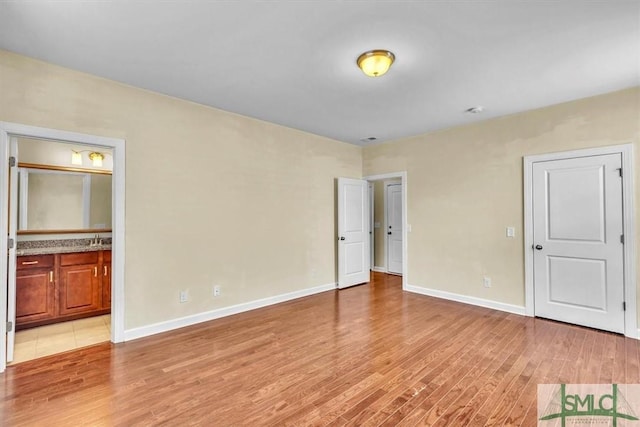 unfurnished bedroom with sink, ensuite bath, and light wood-type flooring