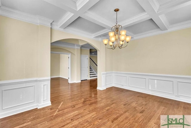 unfurnished dining area with wood-type flooring, coffered ceiling, a chandelier, and beam ceiling