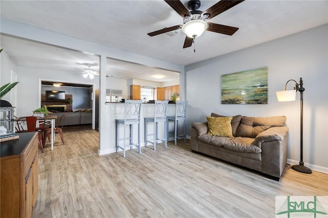 living room featuring a brick fireplace, ceiling fan, and light hardwood / wood-style flooring