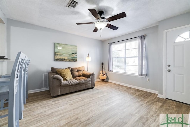 living room featuring ceiling fan, a textured ceiling, and light wood-type flooring