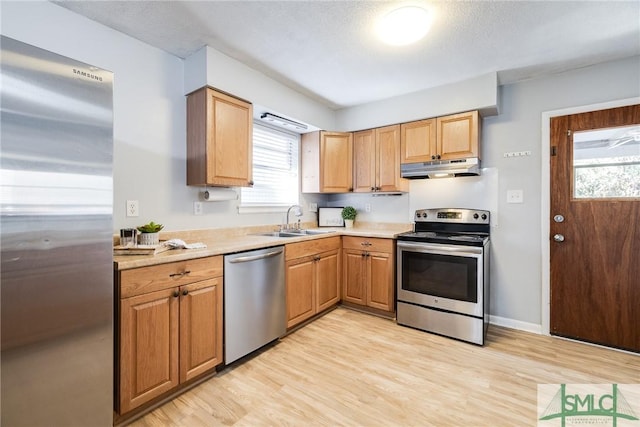 kitchen with stainless steel appliances, sink, a textured ceiling, and light wood-type flooring